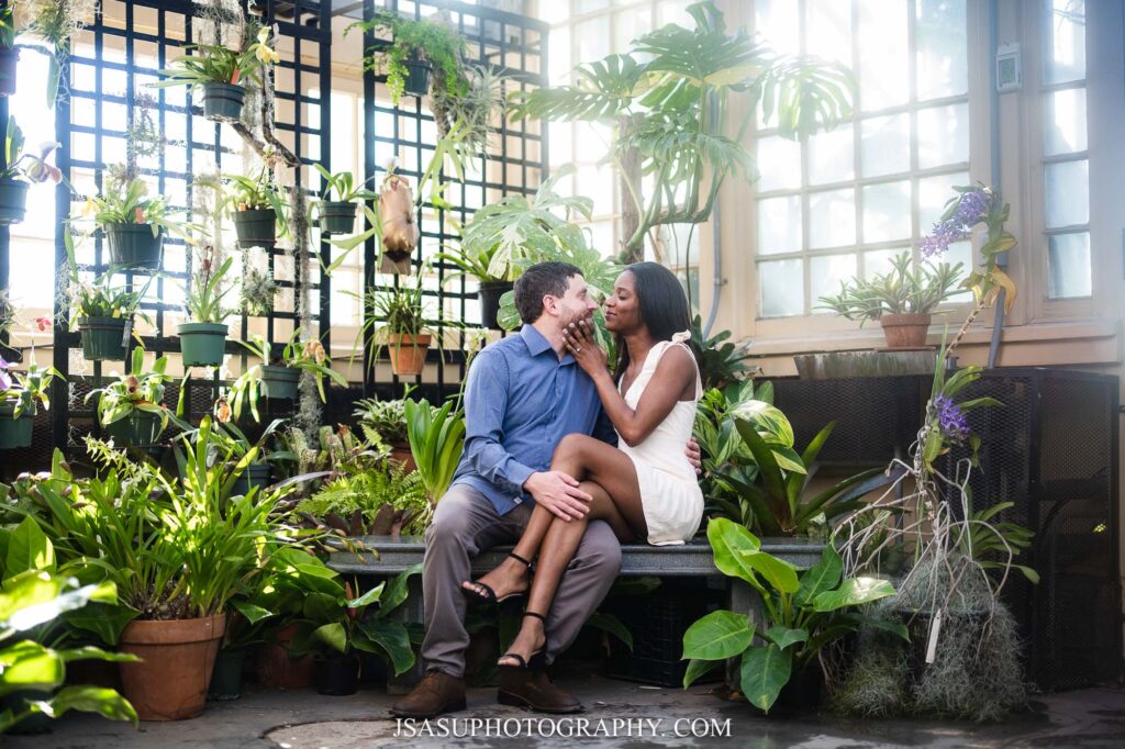 a couple sits on a bench surrounded by foliage at Rawlings Conservatory in Baltimore, MD 
