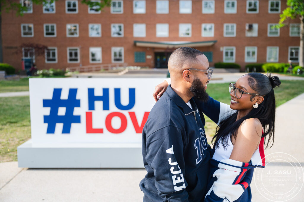 in The Upper Quad of Howard University, a couple wearing Howard University branded clothing, poses for a kiss. 
