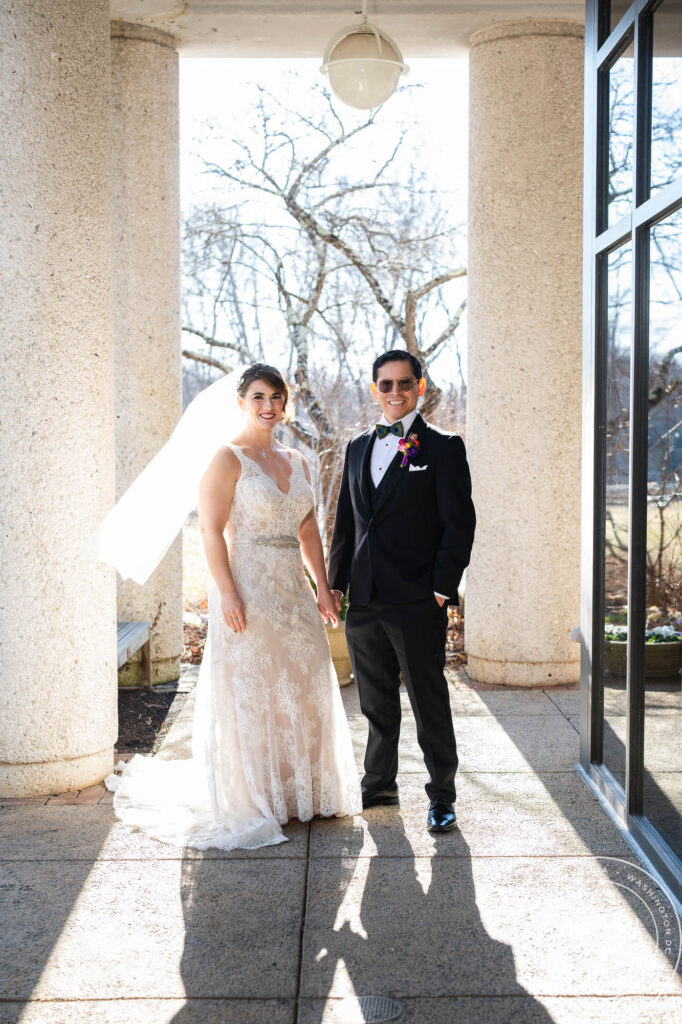 a man in a tuxedo and a woman in a a wedding dress pose for a wedding portrait on wedding day at the atrium at meadowlark botanical gardens