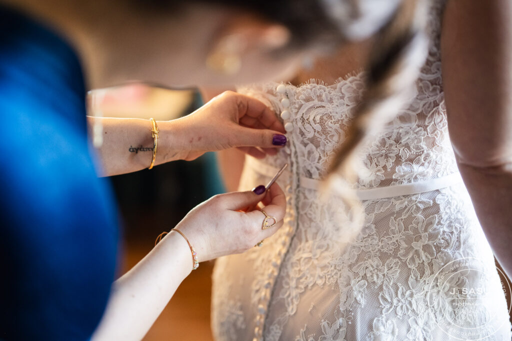 one woman helps another put on the buttons on the back of her wedding gown before her wedding